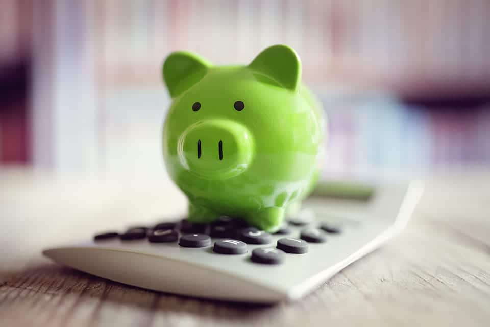 green piggy bank on top of a calculator on a wooden desk