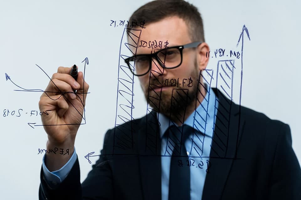 employee with glasses writing with a dry erase pen on a clear board